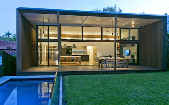 Rear view of contemporary intercity home in Brisbane showing backyard grass, pool, rear deck and extensive glass sliders opening up the kitchen and living areas